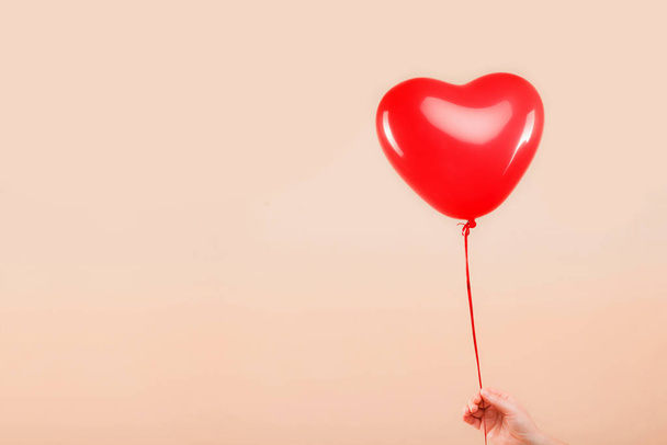 Kadın eli kırmızı kauçuk, şişme kalp şeklinde balon tutuyor. Aşk, ilişki, sevgililer günü ve doğum günü kutlaması konsepti. Stüdyo görüntüsü boş kopya alanı olan bulanık bir arkaplan üzerinde - Fotoğraf, Görsel