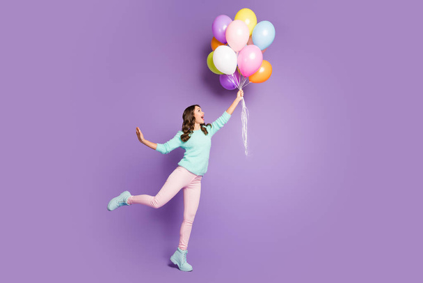 Full body photo of crazy funky feminine girl hold hand catch many baloons flying sky scream wow omg wear soft pink pastel trousers pants footwear isolated over violet color background - 写真・画像
