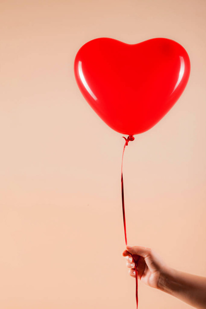 Female hand holds red rubber inflatable heart shape balloon. Love, relationship, valentines day and birthday celebration concept. Studio shot on an abstract blurred background with blank copy space - Photo, Image