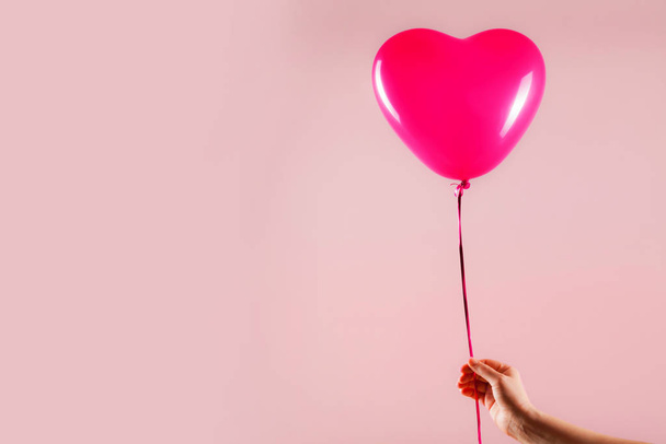 Female hand holds red rubber inflatable heart shape balloon. Love, relationship, valentines day and birthday celebration concept. Studio shot on an abstract blurred background with blank copy space - Φωτογραφία, εικόνα