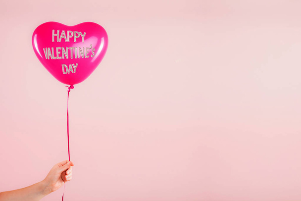 A mão fêmea segura o balão inflável da forma do coração da borracha vermelha. Amor, relacionamento, dia dos namorados e conceito de celebração de aniversário. Estúdio filmado em um fundo embaçado abstrato com espaço em branco
 - Foto, Imagem