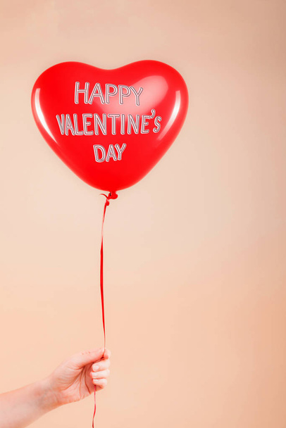 Female hand holds red rubber inflatable heart shape balloon. Love, relationship, valentines day and birthday celebration concept. Studio shot on an abstract blurred background with blank copy space - Фото, изображение