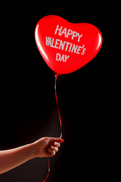 Female hand holds red rubber inflatable heart shape balloon. Love, relationship, valentines day and birthday celebration concept. Studio shot on an abstract blurred background with blank copy space - Фото, изображение