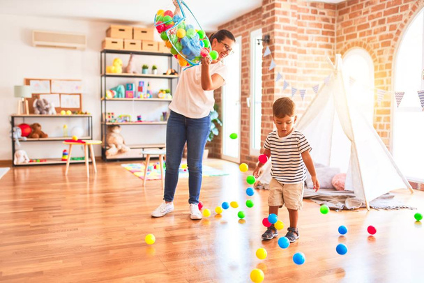 Kaunis opettaja ja lapsi poika leikkivät värillisillä pienillä palloilla päiväkodissa
 - Valokuva, kuva