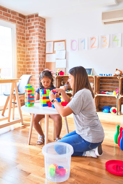 Beautiful teacher and toddler girl playing with construction blocks bulding tower at kindergarten - Photo, Image
