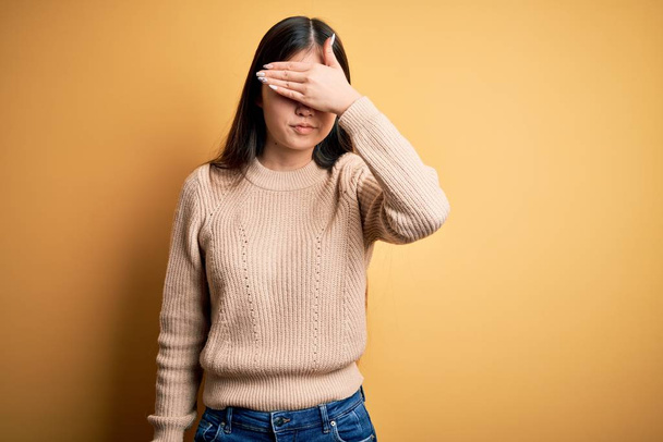 Young beautiful asian woman wearing casual sweater over yellow isolated background covering eyes with hand, looking serious and sad. Sightless, hiding and rejection concept - Foto, Bild