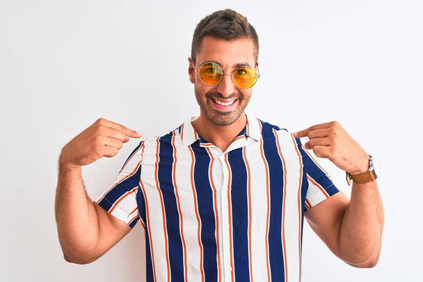 Mladý pohledný muž v letních slunečních brýlích na izolovaném pozadí vypadá sebevědomě s úsměvem na tváři, ukazuje na sebe s prsty hrdý a šťastný. - Fotografie, Obrázek