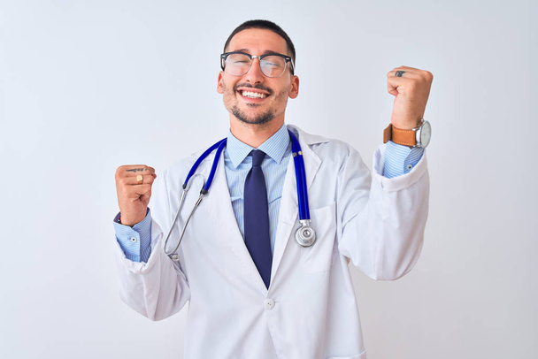 Young doctor man wearing stethoscope over isolated background celebrating surprised and amazed for success with arms raised and eyes closed. Winner concept. - Fotografie, Obrázek