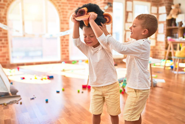Adorables jumeaux blonds jouant avec un masque de singe autour de beaucoup de jouets à la maternelle
 - Photo, image