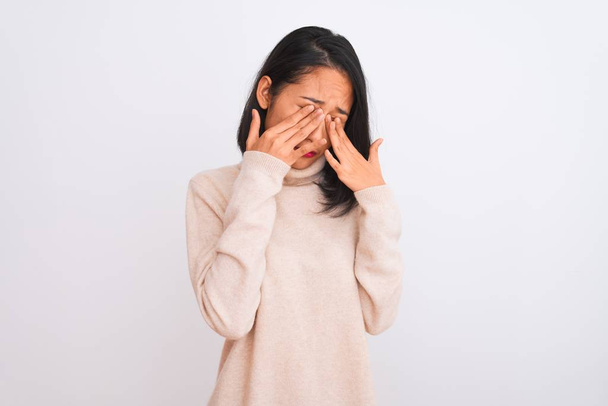 junge Chinesin mit Rollkragenpullover, die vor isoliertem weißem Hintergrund steht, reibt sich die Augen vor Müdigkeit und Kopfschmerzen, schläfriger und müder Miene. Sehschwäche - Foto, Bild