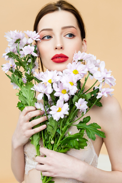 pretty girl looking away and holding blooming chrysanthemum flowers isolated on beige  - Fotografie, Obrázek