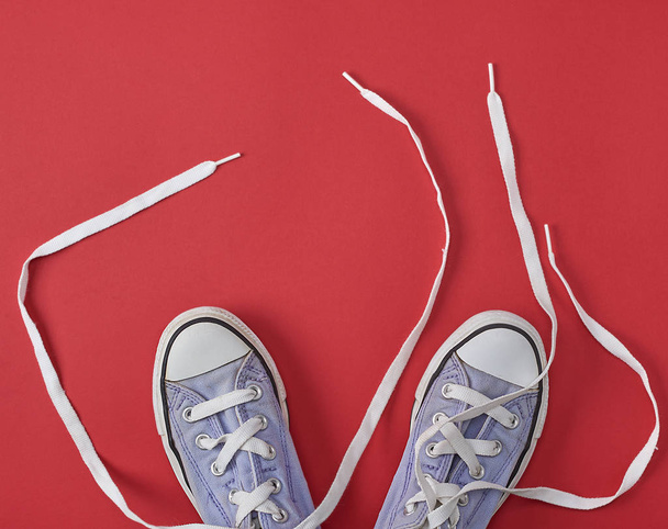 viejas zapatillas desgastadas con cordones blancos desatados sobre un fondo rojo, vista superior
 - Foto, imagen