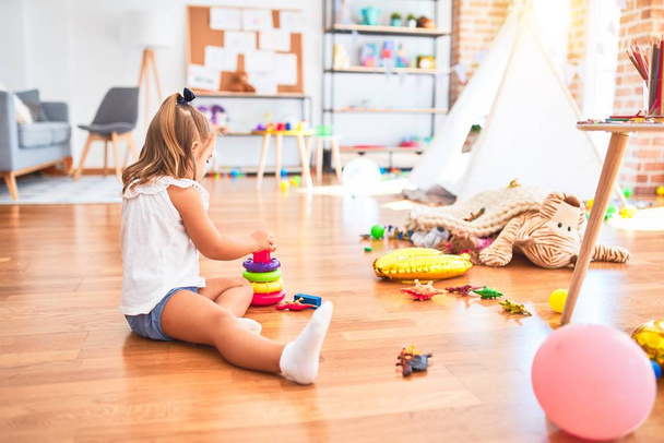 Молодая красивая блондинка девочка наслаждается игрой школы с игрушками в детском саду, улыбаясь счастливо играть с интеллигенции игрушки дома
 - Фото, изображение