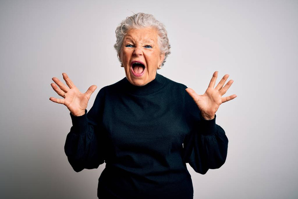 Senior beautiful woman wearing casual black sweater standing over isolated white background crazy and mad shouting and yelling with aggressive expression and arms raised. Frustration concept. - Foto, Imagem