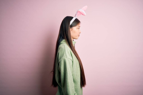 Young asian woman wearing cute easter bunny ears over pink background looking to side, relax profile pose with natural face with confident smile. - Photo, Image