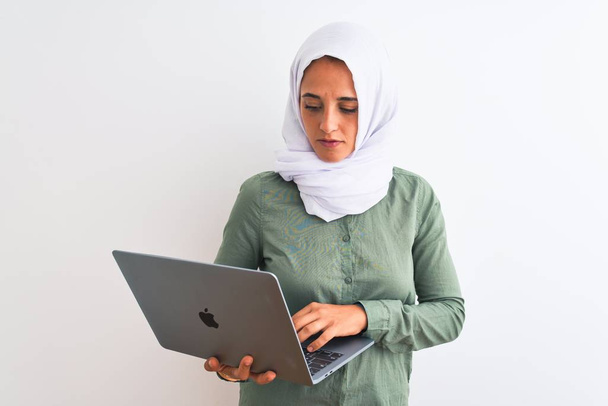 Mladá arabská podnikatelka nosí hidžáb pomocí notebooku přes izolované pozadí s sebejistým výrazem na chytré tváři myšlení vážné - Fotografie, Obrázek