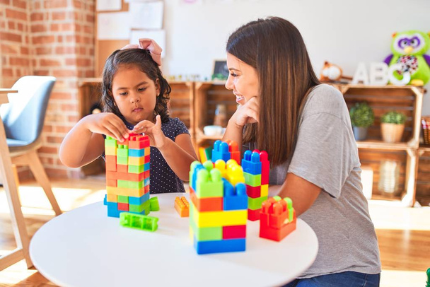 Piękny nauczyciel i dziewczynka maluch gra z bloków budowlanych bulding wieży w przedszkolu - Zdjęcie, obraz