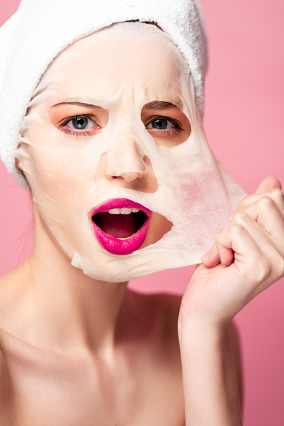choqué jeune femme touchant masque facial isolé sur rose
  - Photo, image