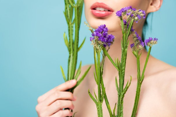 cropped view of naked girl holding limonium flowers isolated on blue  - Foto, Imagem
