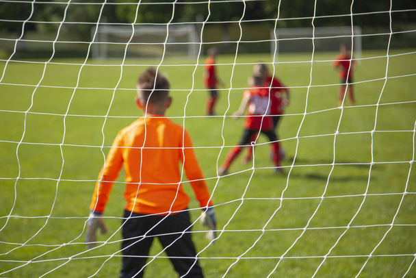 Goalkeeper catches the ball. Goal net in focus. Sports competition. Children's football on the field. Physical development. Children's sport. Sleight of hand. Ball Championship. - Photo, image