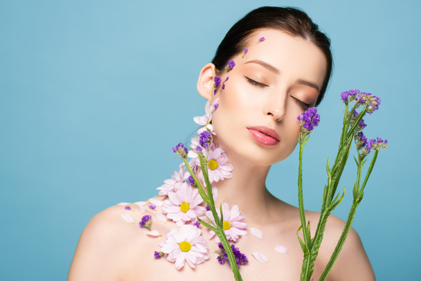 naked young woman with closed eyes near blooming flowers isolated on blue  - Fotoğraf, Görsel