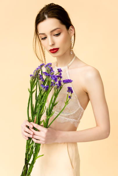 attractive woman looking at purple limonium flowers isolated on beige  - Foto, afbeelding