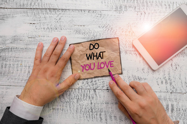 Word writing text Do What You Love. Business photo showcasing Make enjoyable things do activities with motivation Hand hold note paper near writing equipment and modern smartphone device - Photo, Image