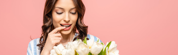 panoramic shot of happy girl touching lip while holding bouquet of white tulips isolated on pink - Φωτογραφία, εικόνα