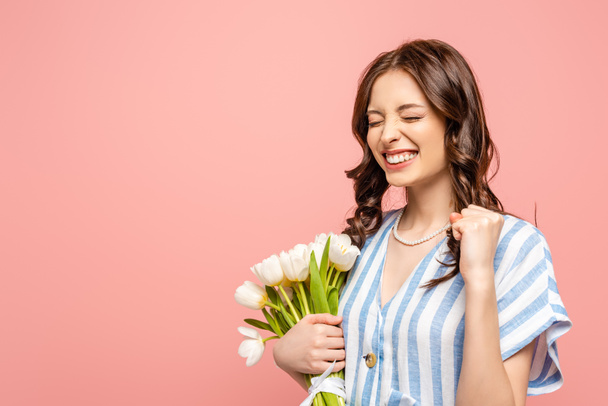 excited girl showing yes gesture while holding bouquet of white tulips isolated on pink - Zdjęcie, obraz