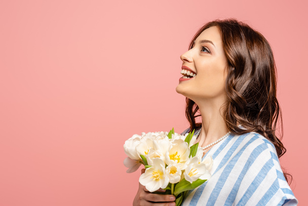 happy girl looking up while holding bouquet of white tulips isolated on pink - Foto, afbeelding