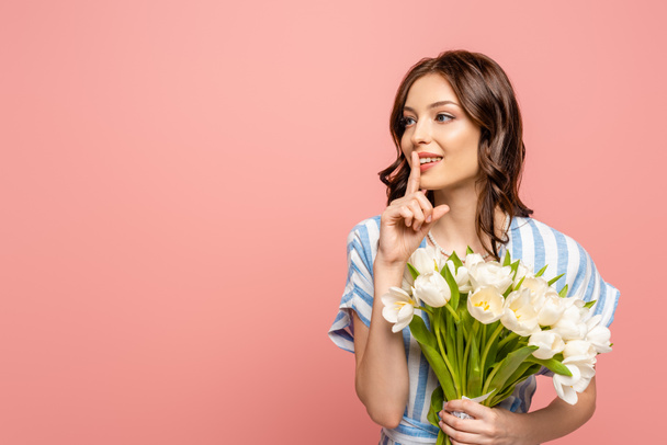 attractive girl showing hush gesture while holding bouquet of white tulips isolated on pink - Photo, Image