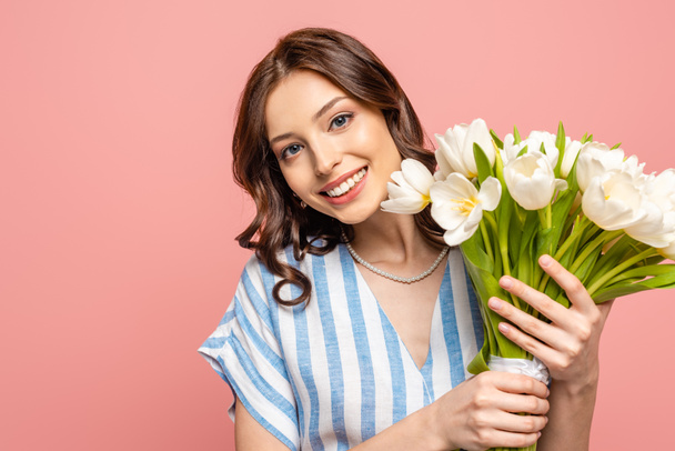 happy girl smiling at camera while holding bouquet of white tulips isolated on pink - Valokuva, kuva