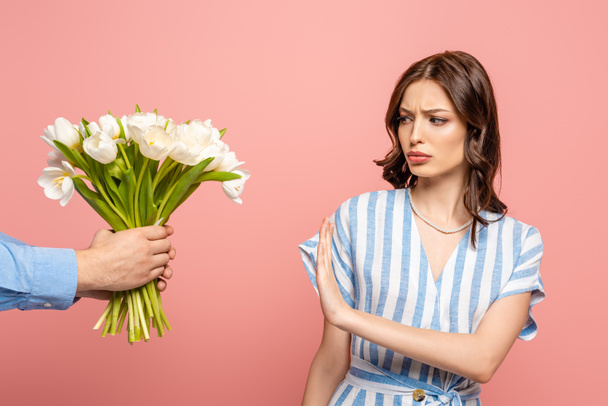 vista parcial del hombre que presenta ramo de tulipanes blancos a chica disgustada que no muestra ningún gesto aislado en rosa
 - Foto, Imagen