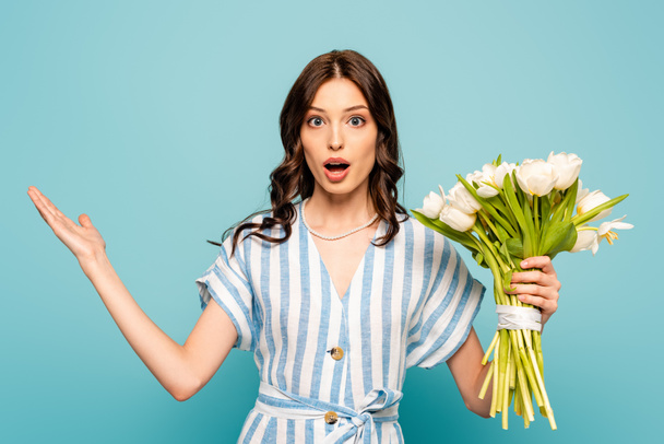 sorprendió a la joven mujer sosteniendo ramo de tulipanes mientras estaba de pie con el brazo abierto aislado en azul
 - Foto, Imagen