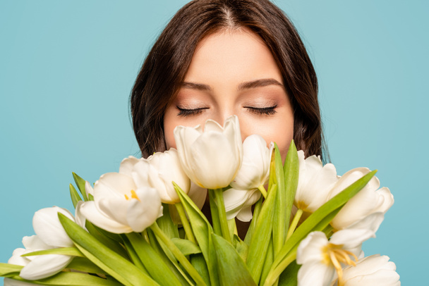 bela jovem desfrutando de sabor de tulipas brancas com olhos fechados isolados em azul
 - Foto, Imagem