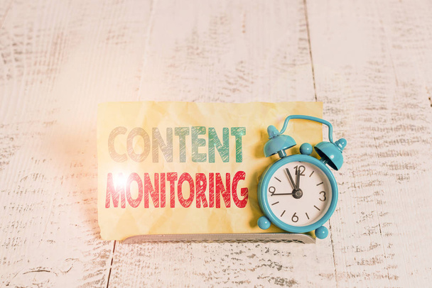 Tekst schrijven Content Monitoring. Zakelijke foto presentatie van een tool om vermeldingen van hun organisatie te identificeren Mini blauwe wekker staan gekanteld boven bufferdraad in de voorkant van briefpapier - Foto, afbeelding