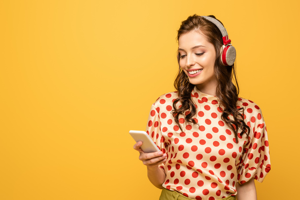 happy young woman in wireless headphones chatting on smartphone isolated on yellow - Photo, Image