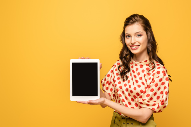 cheerful young woman smiling at camera while showing digital tablet with blank screen isolated on yellow - Foto, afbeelding
