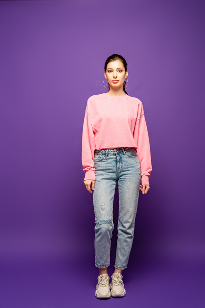 full length view of pretty, confident girl looking at camera while standing on purple background - Φωτογραφία, εικόνα
