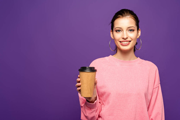 pretty girl smiling at camera while holding coffee to go isolated on purple - Zdjęcie, obraz