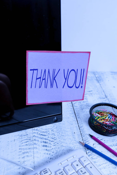 Handwriting text writing Thank You. Conceptual photo polite expression used when acknowledging gift service compliment Note paper taped to black computer screen near keyboard and stationary - Фото, зображення