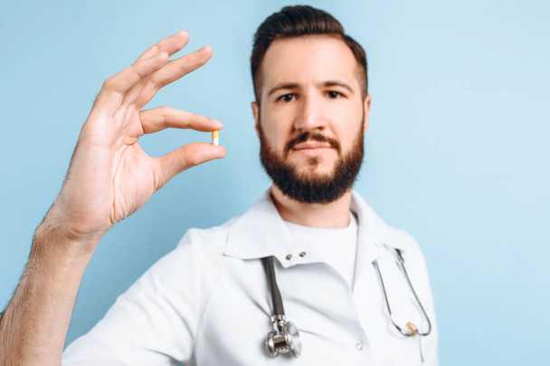 Happy confident male doctor holding a pill on a light blue backg - Fotó, kép