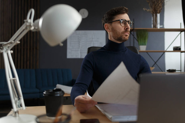 Architect working in office with blueprints.Engineer inspect architectural plan, sketching a construction project.Portrait of handsome bearded man sitting at workplace. Business construction concept - Foto, imagen