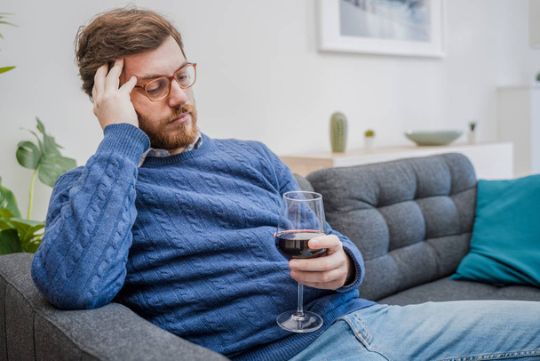 Retrato del hombre con bebida alcohólica sentado en el sofá en casa - Foto, Imagen