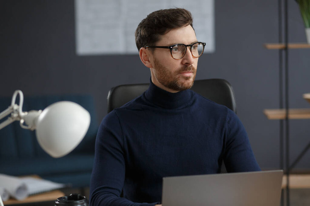 Architect working in office with laptop. Business portrait of handsome bearded man wearing eyeglasses sitting at workplace. Confident businessman became successful. Business concept - Foto, immagini