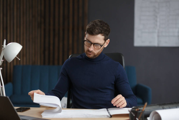 Architect working in office with blueprints.Engineer inspect architectural plan, sketching a construction project.Portrait of handsome bearded man sitting at workplace. Business construction concept - 写真・画像
