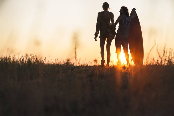 Silhouette of young couple holding surfboard and looking at sunset - Foto, Imagem