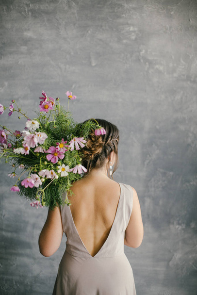 A young Beautiful Girl in a Pink Dress Holding a Delicate Bouquet of Flowers on a Gray Background - Photo, Image