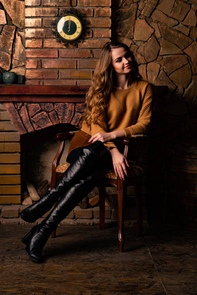 atractiva mujer joven sentada en silla cerca de la chimenea en estudio   - Foto, Imagen