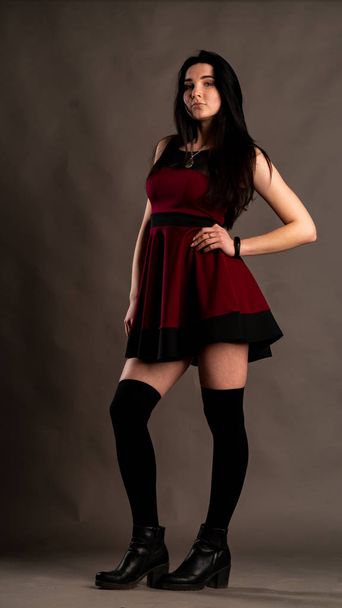 Pretty young sexy model female with dark hair in red dress posing in dark studio. - Photo, Image